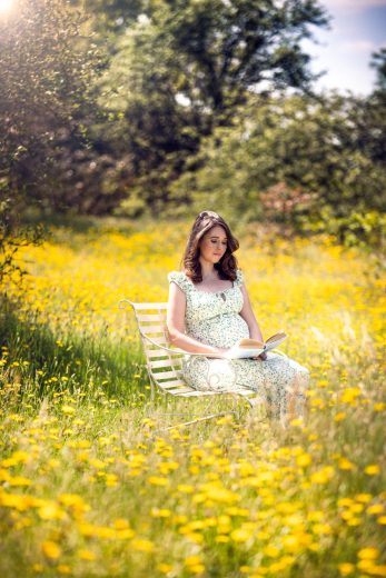 Maternity photo of mother to be reading a book on a bench surrounded by lovely yellow flowers