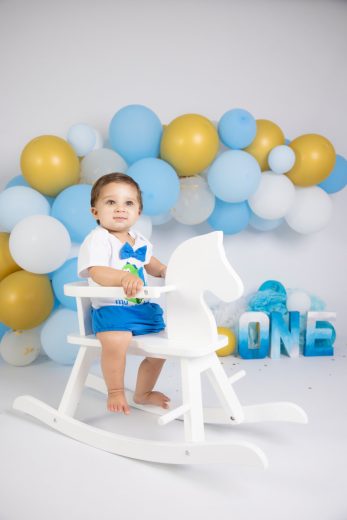 Little boy on rocking horse with balloon arch in the background